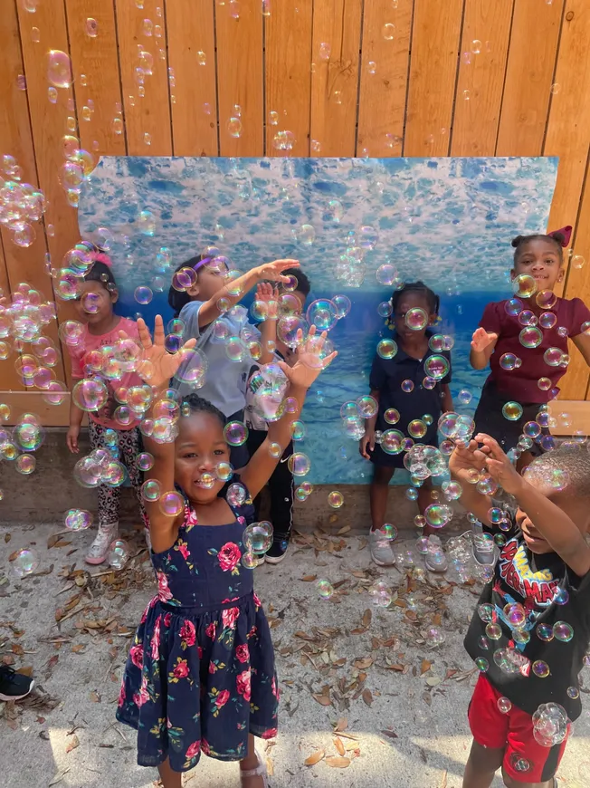 A group of children playing with bubbles in front of a painting.