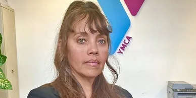 A woman with long hair and bangs is standing in front of an ymca sign.