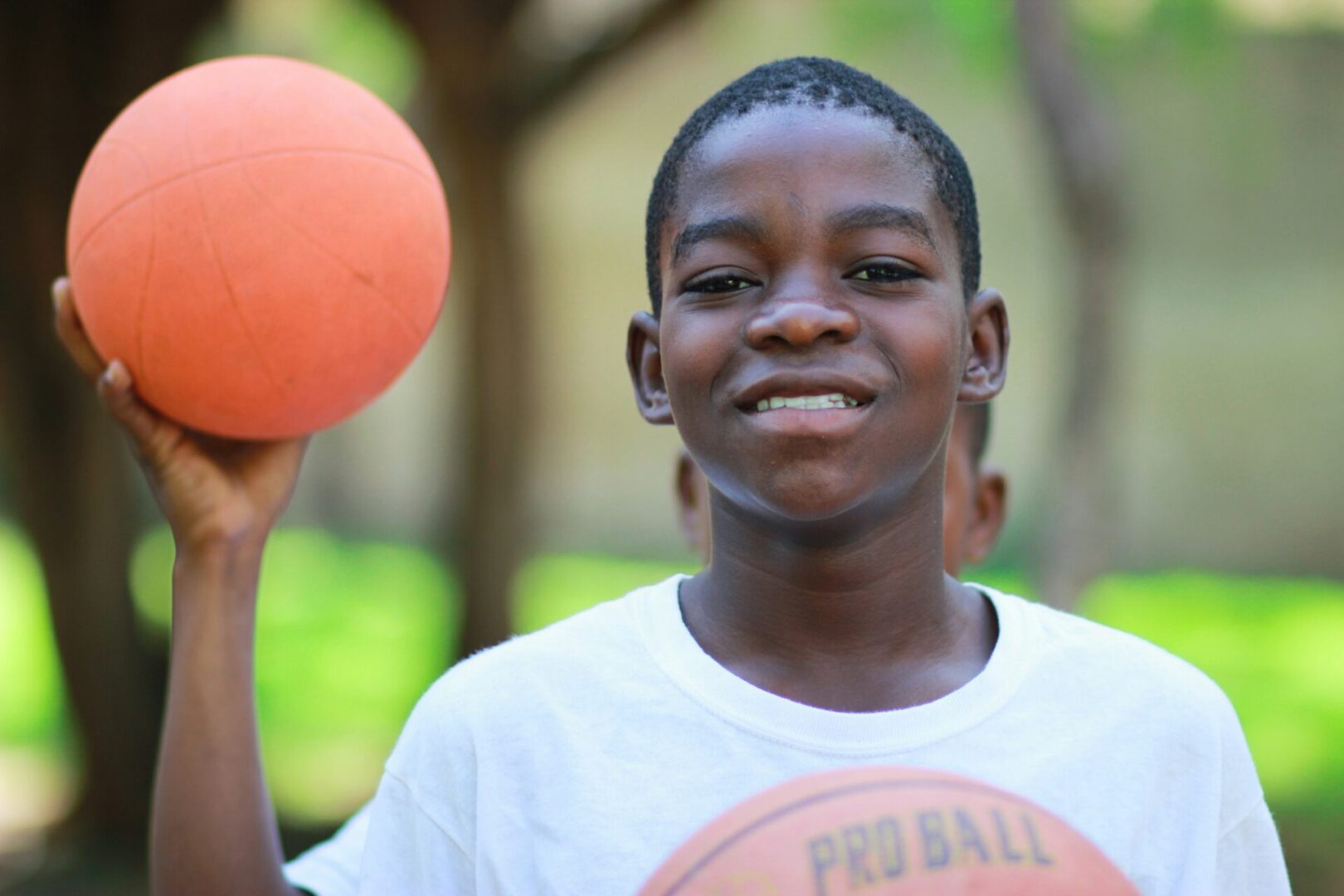 A small boy holding a basket ball and wearing a white tshirt.