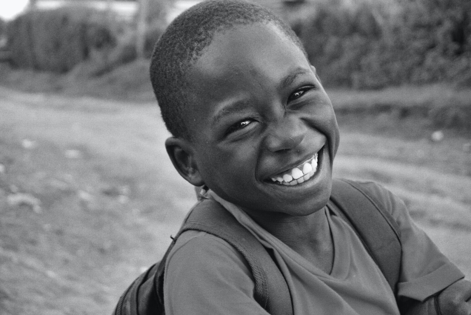 A black and white image of a small boy hanging a bag and smiling